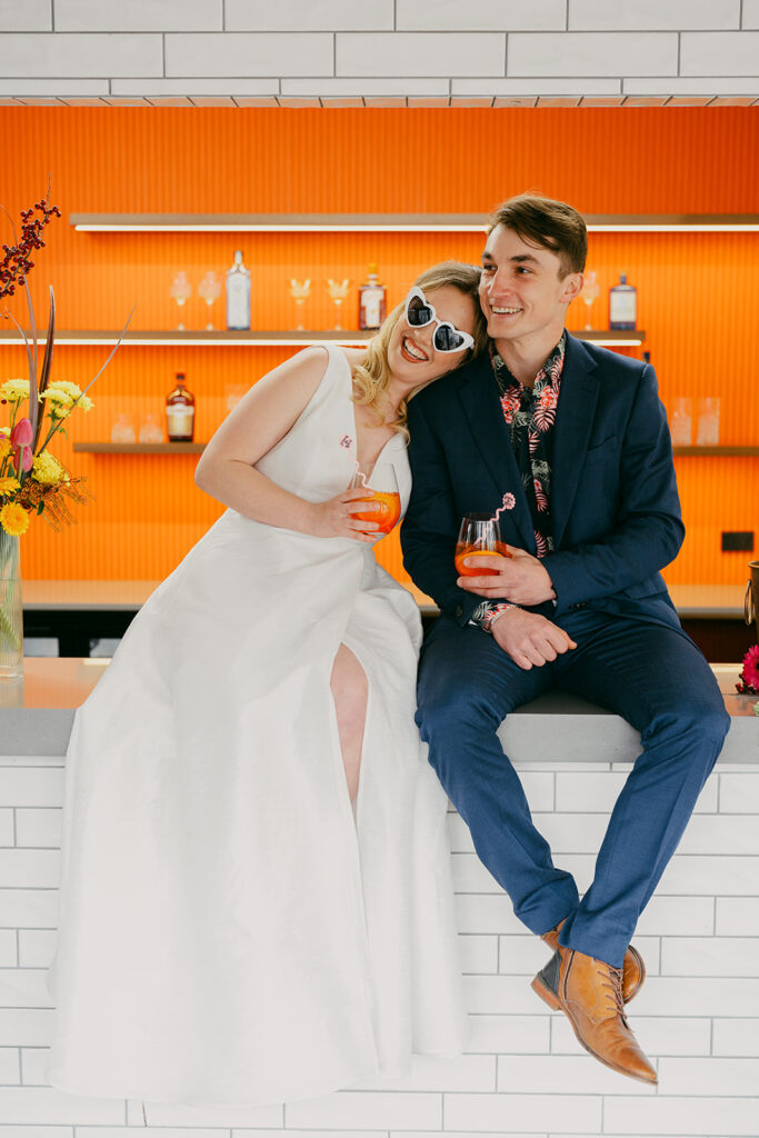 Bride and Groom sitting on the bar. Her head is on his shoulder and they are smiling with joy