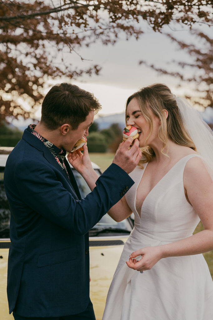 Bride and Groom feeding each other pink frosted cupcakes outside in the afternoon light of Wānaka