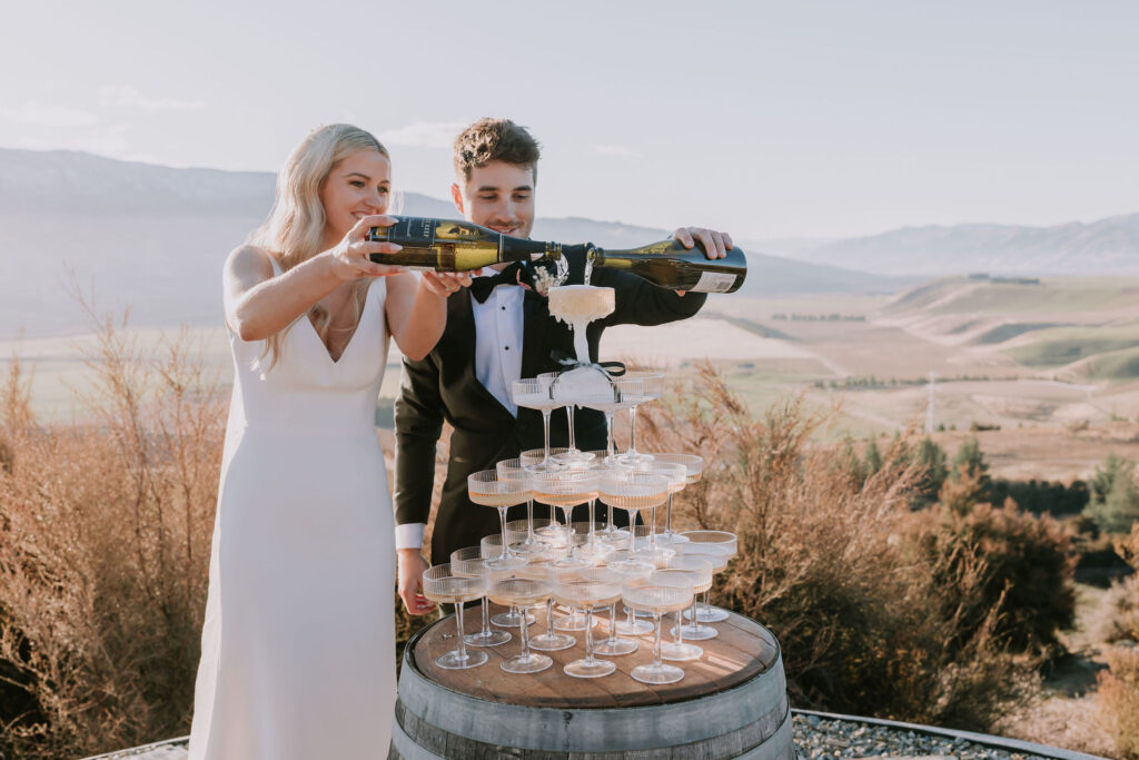 Bride and Groom pouring the champagne tower on a wine barrel in Central Otago