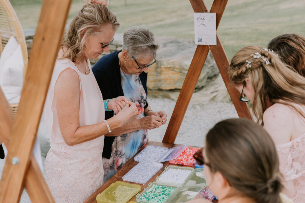 Wedding guests creating colourful kandi bracelets at a DIY activity station during cocktail hour.