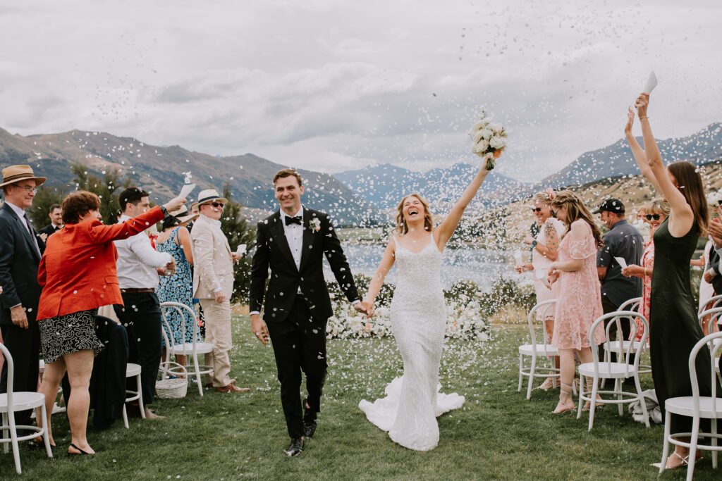 Bride and groom walking back down the aisle under a shower of petals, smiling and celebrating with guests.