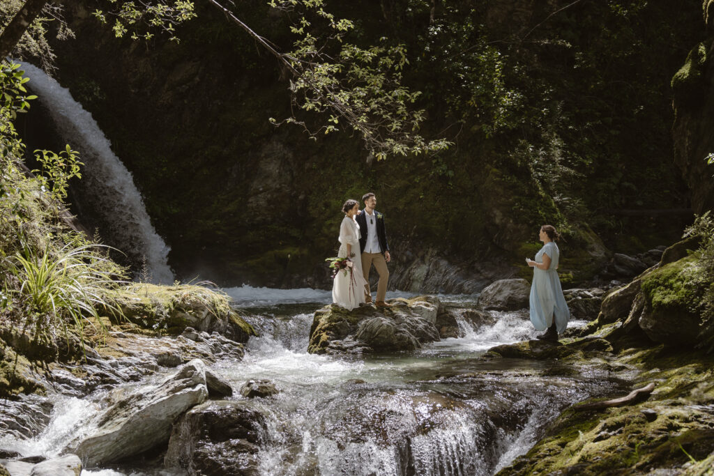 Bride and groom standing on rocks by a waterfall during an intimate adventure elopement ceremony.