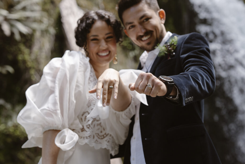 Bride and groom showing wedding rings in a forest waterfall setting, Queenstown adventure elopement.