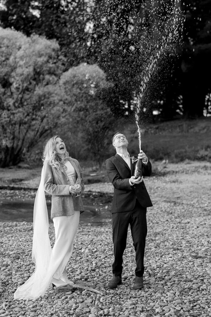 Black-and-white image of couple celebrating with champagne spray during their intimate elopement.