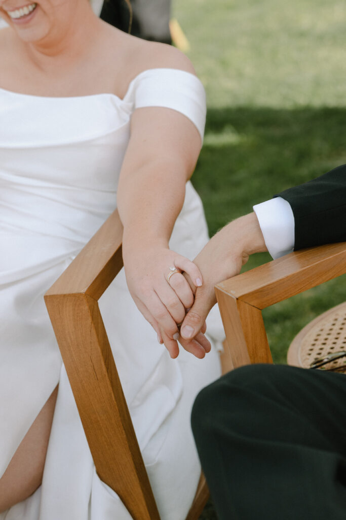 Close-up of the bride and groom holding hands, showing their wedding rings