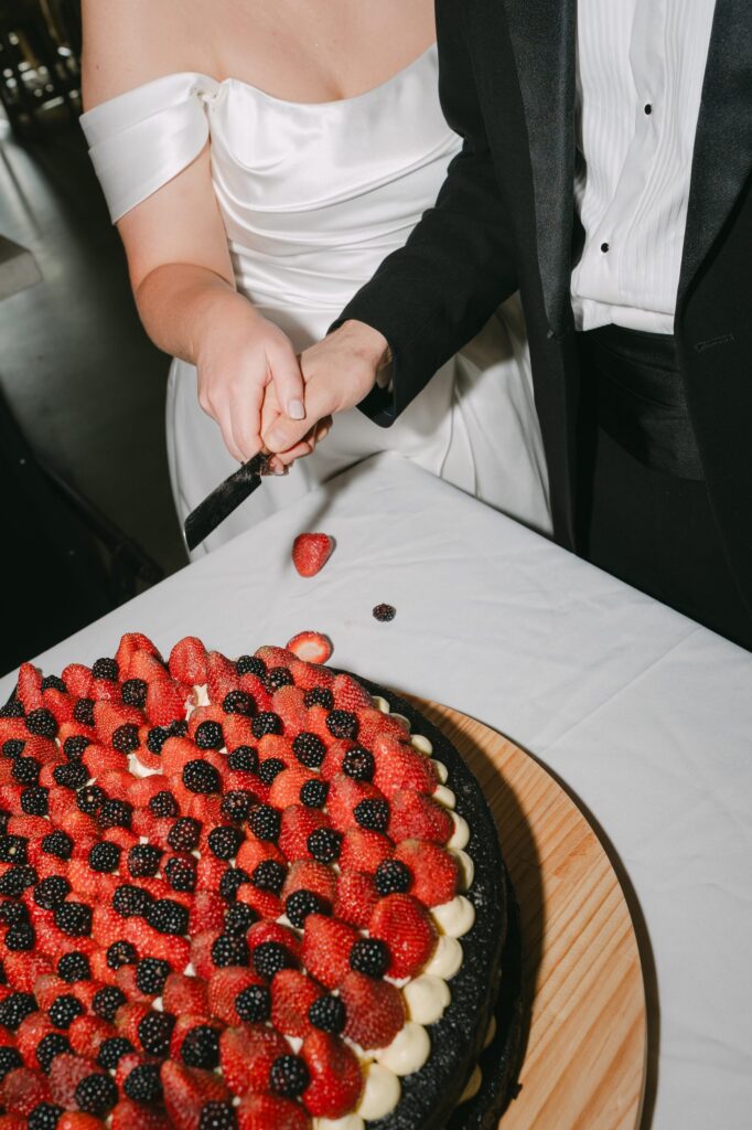 Bride and groom cutting their berry-topped wedding cake together, close-up