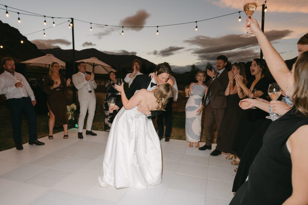 Bride and groom dancing at their reception as guests cheer and raise their glasses
